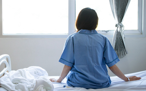Back view of mental health patient sitting on a hospital bed, looking out the window. 