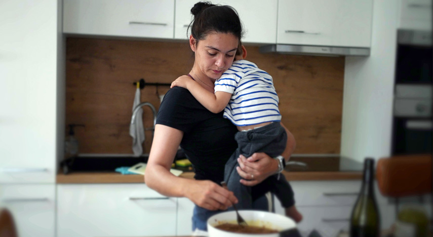 mother holding baby while cooking stew