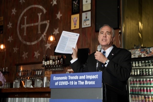 Comptroller DiNapoli behind a podium holding a report at a press conference.