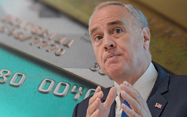 New York State Comptroller Thomas P. DiNapoli with a stack of colorful credit cards behind him. 