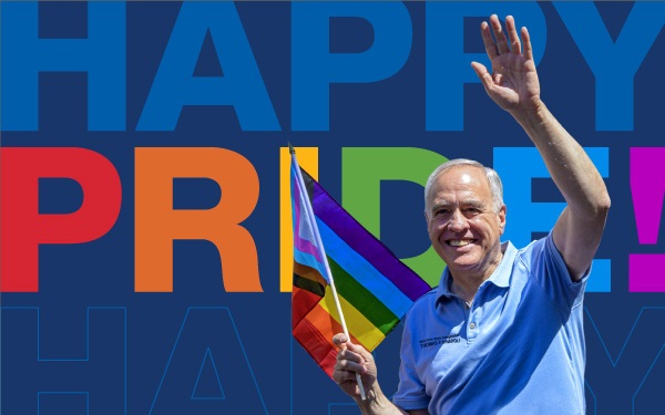 Comptroller Thomas P. DiNapoli waving a Pride banner with the words “Happy Pride” in the background.