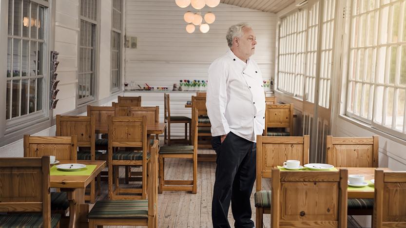 Man in chef jacket standing in empty restaurant